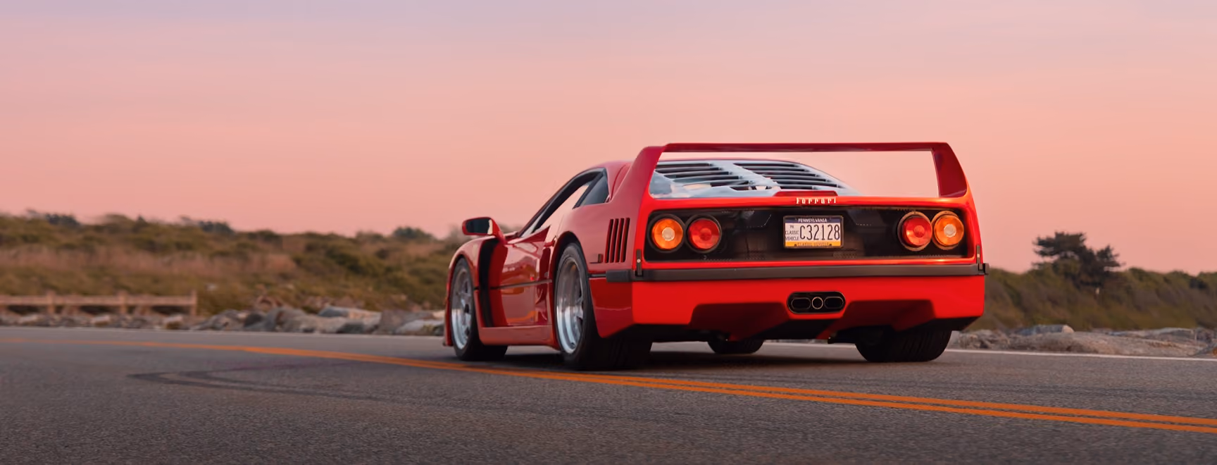 Red Ferrari from behind on an open road at sunset