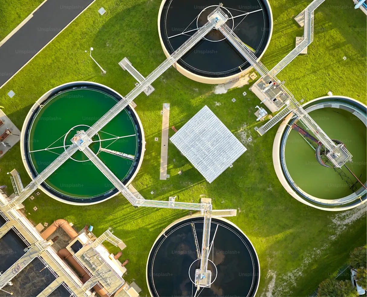 Aerial view of four circular water treatment tanks with connecting walkways on green grass.