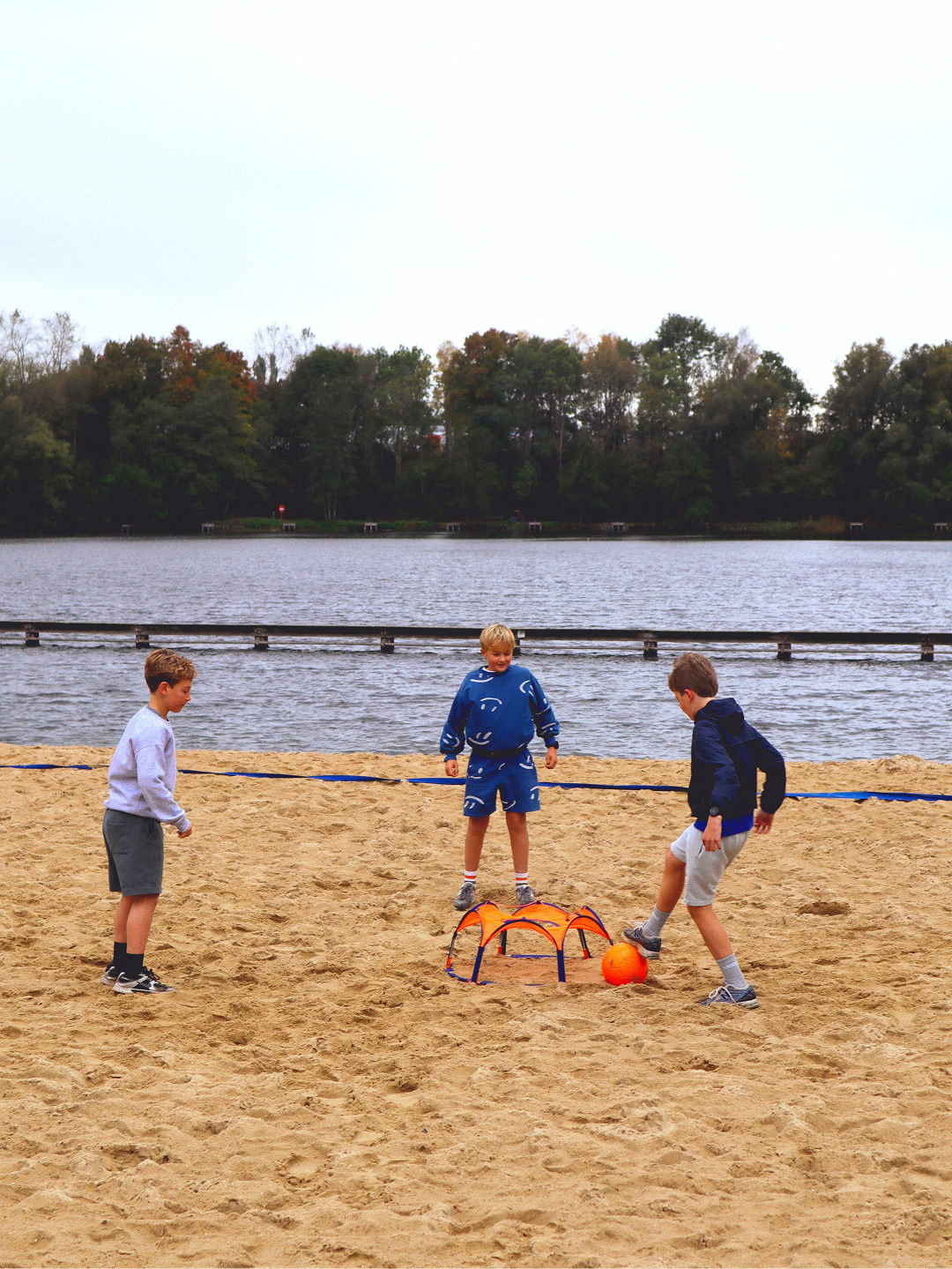 Drie jongens spelen panna op het zand aan een meer, met de oranje Pannaball goal en bal in het midden
