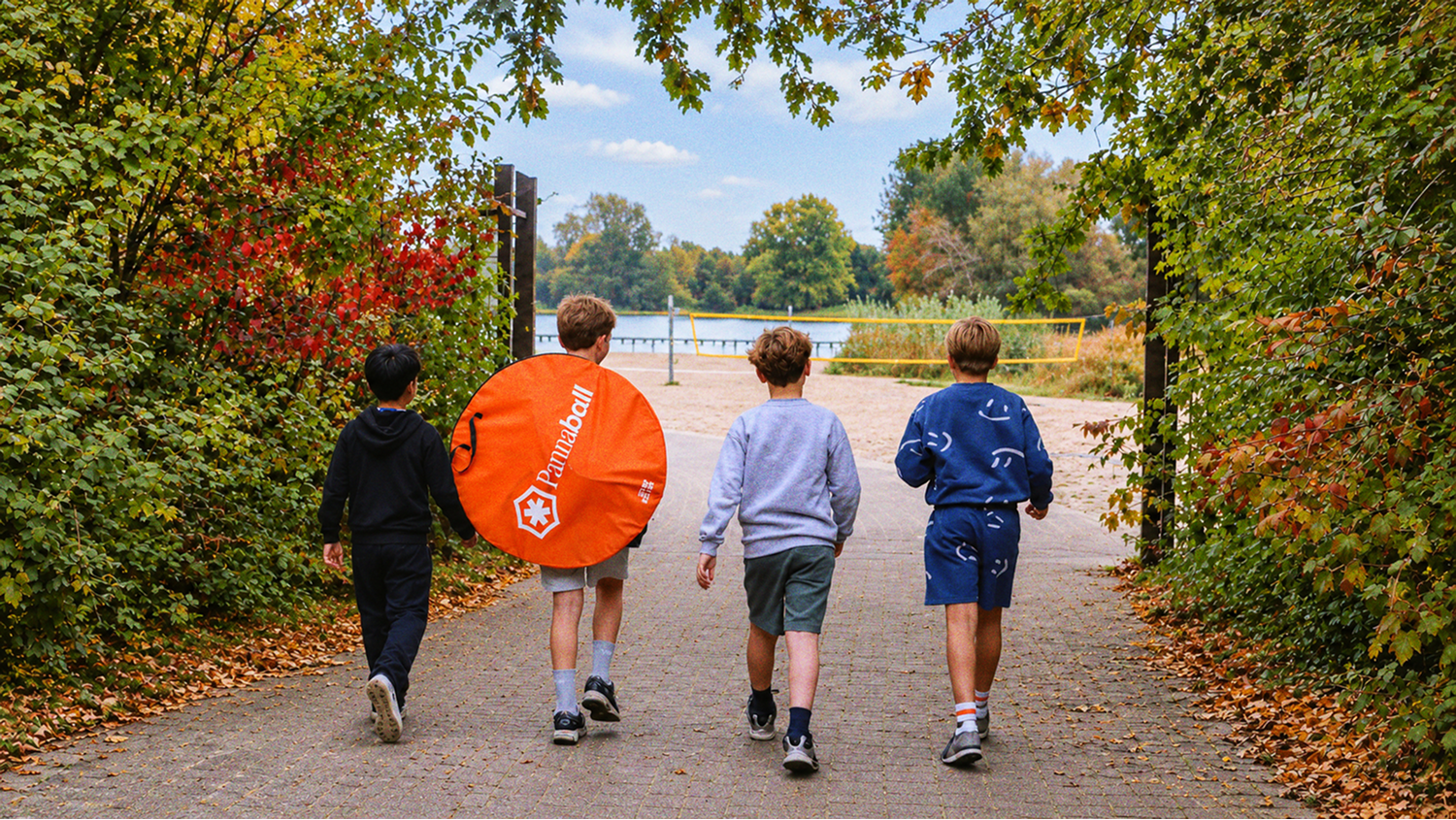 Four boys walking towards a lakeside beach, one carrying the round orange Pannaball carry bag over his shoulder