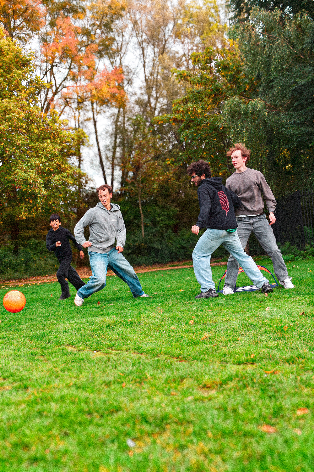 Four young people playing panna on a grass field in a park in autumn, with the Pannaball goal and an orange ball