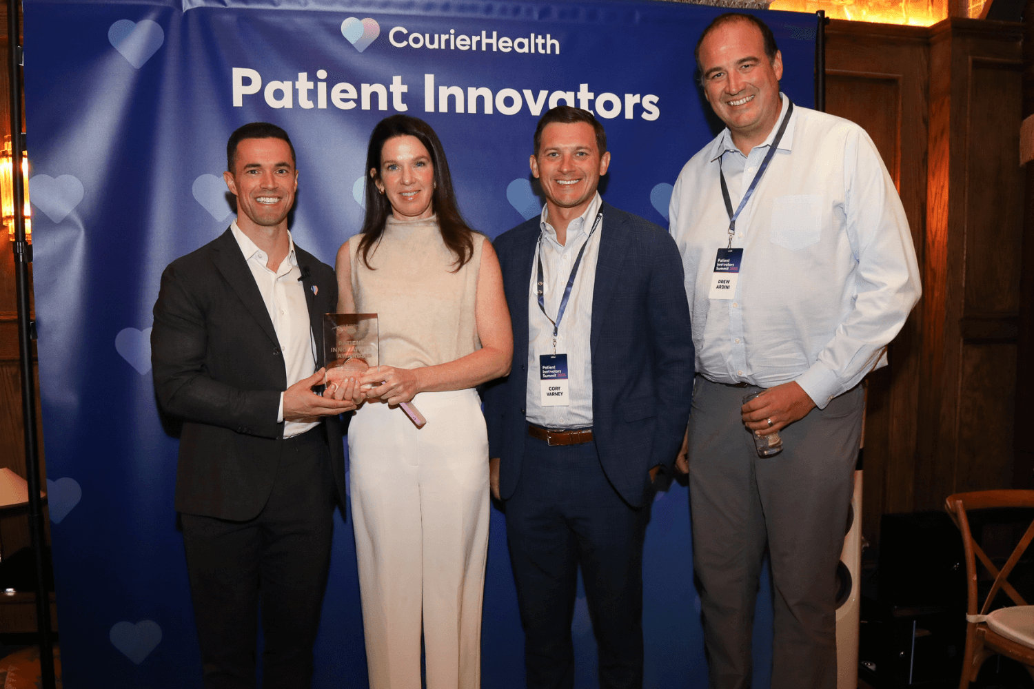 Four people standing in front of a blue backdrop with 'CourierHealth Patient Innovators' text; two individuals in the center hold a transparent plaque, all dressed in business attire and smiling.