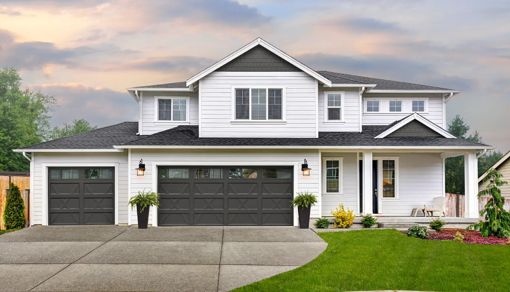 Modern two-story house with three black garage doors, white siding, and a green lawn under a cloudy sky.
