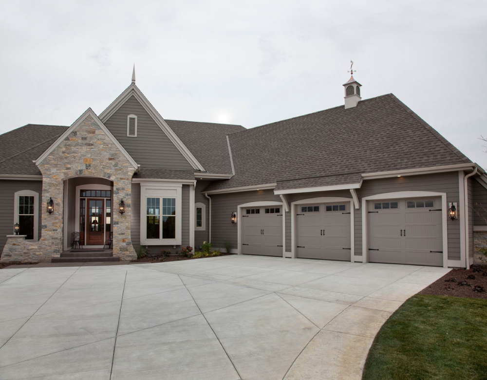 Large modern home with stone facade, three-car garage, gray siding, and concrete driveway.