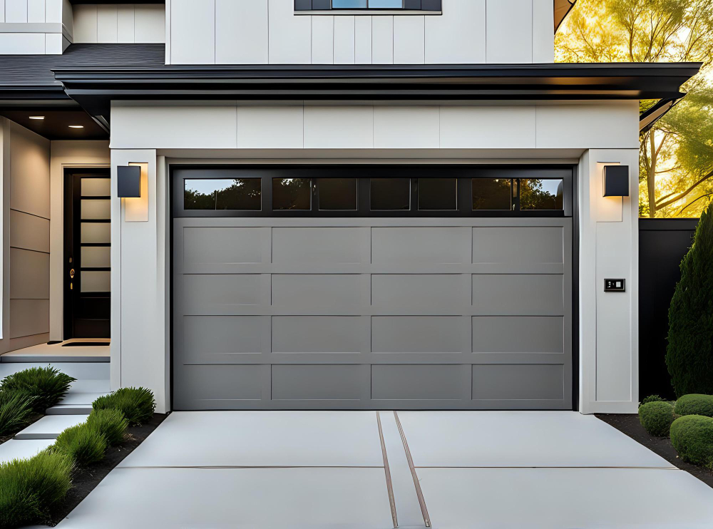 Modern house exterior with gray garage door and side entrance, flanked by outdoor wall lights and greenery.