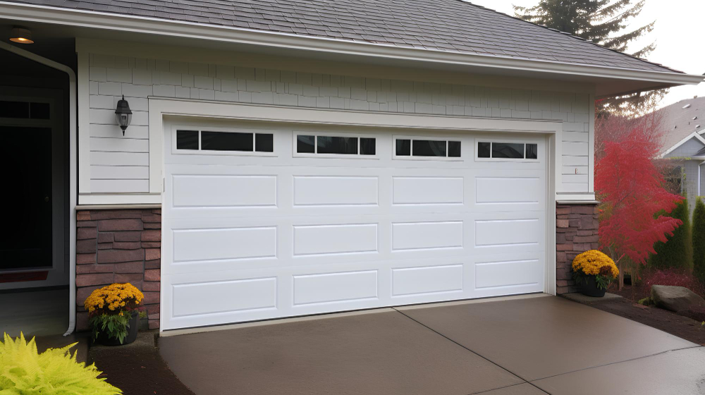 White paneled garage door on a house with stone siding and potted yellow flowers on both sides.