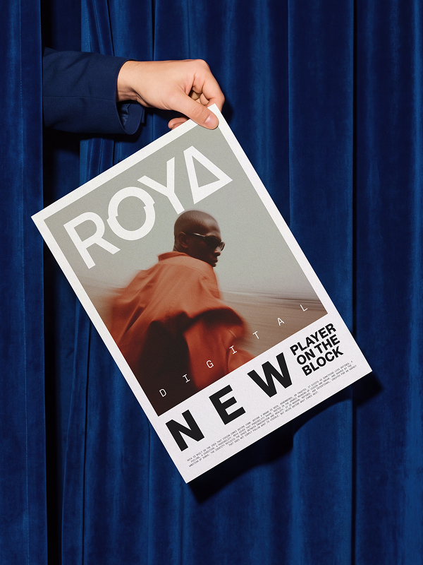 A hand coming from behind the curtain holding a poster showcasing a new agancy by the name of Roya