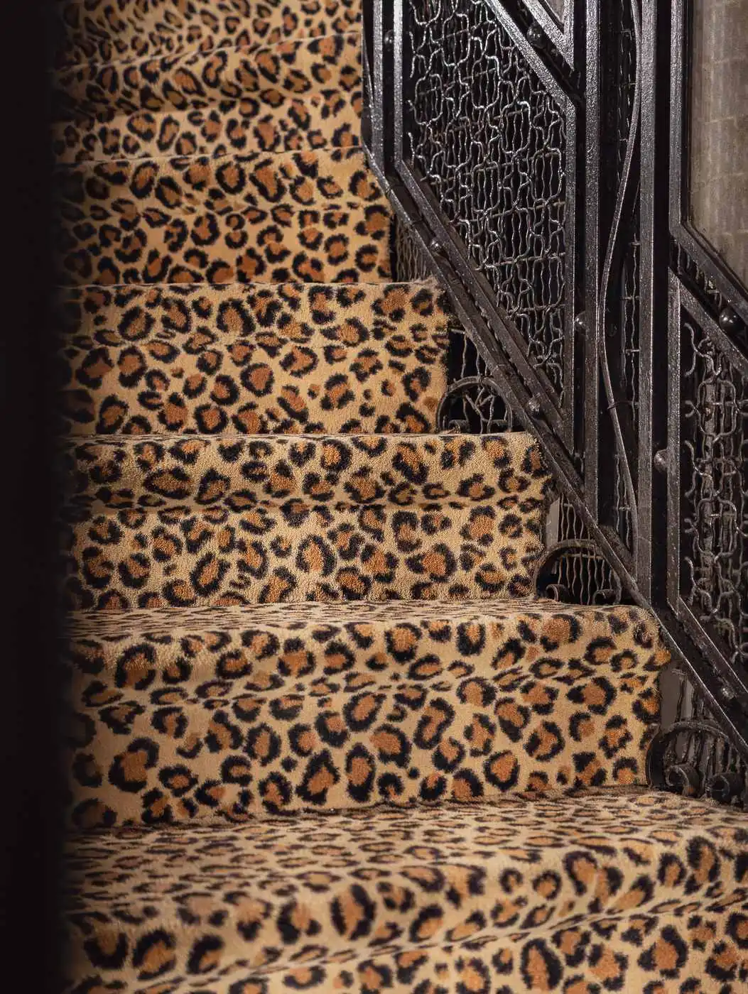 Escalier recouvert d'un tapis à motif léopard avec une balustrade en métal noir ornée de motifs décoratifs.