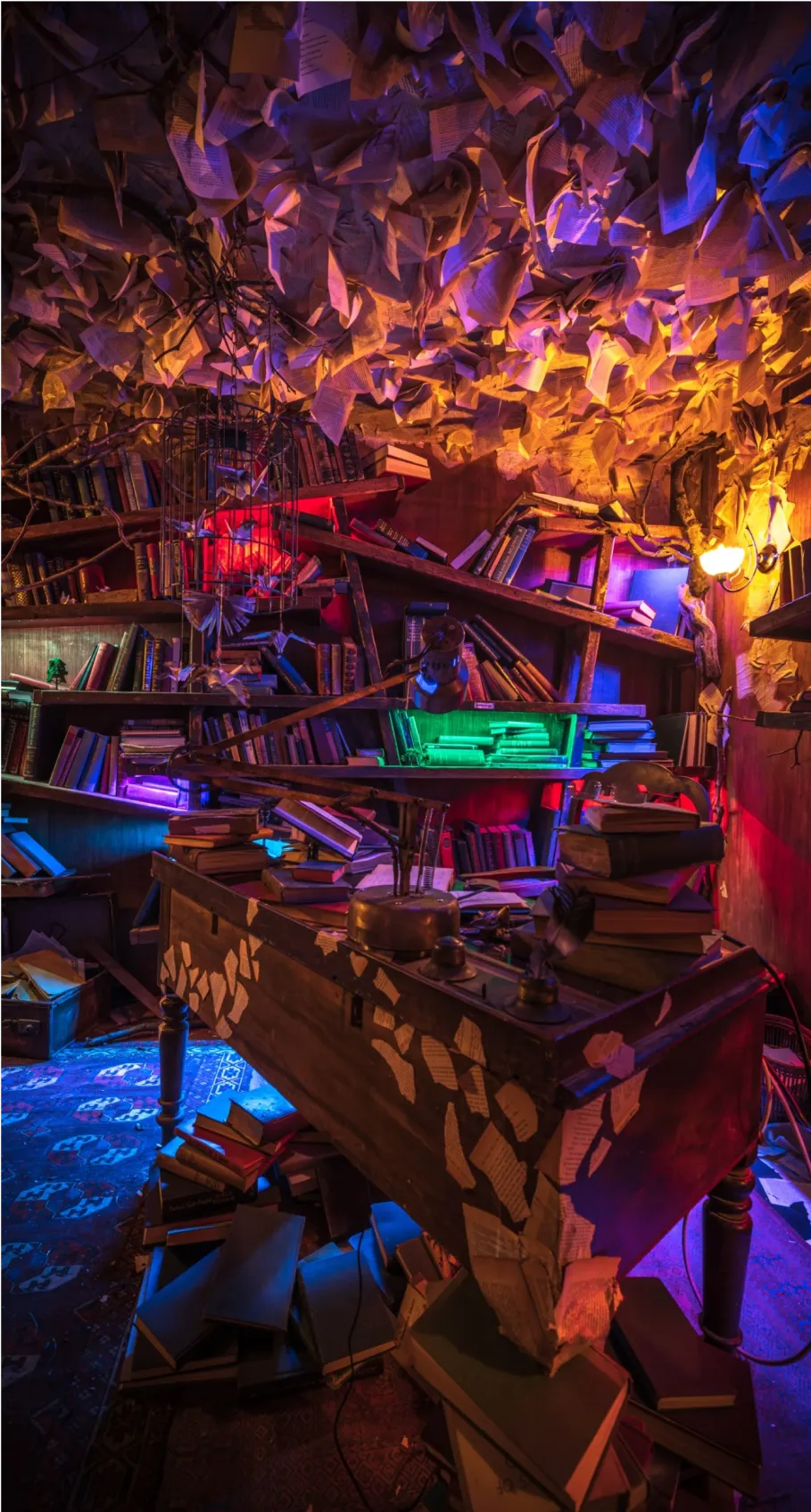 Whimsical library room with scattered books, a vintage desk, and colorful lighting, featuring pages hanging from the ceiling.
