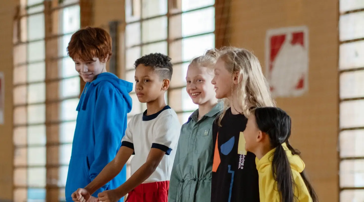 Group of kids smiling and socializing during a youth fitness program in a gym.