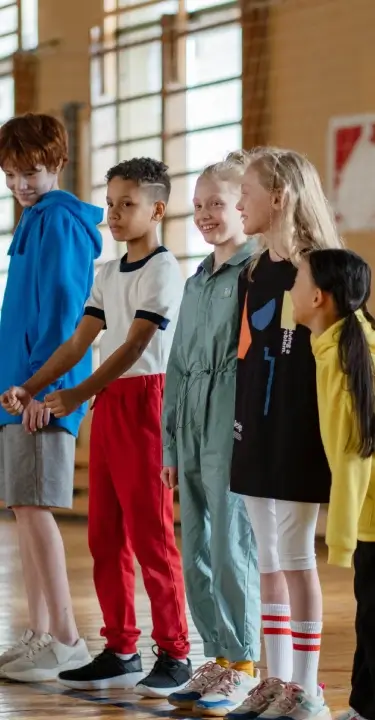 Group of kids smiling and socializing during a youth fitness program in a gym.