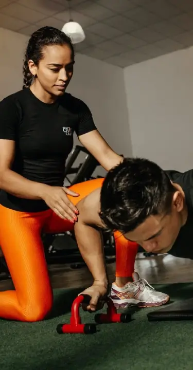 Personal trainer coaching a man through a push-up exercise during a one-on-one gym workout.