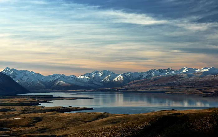 Snow-capped mountain range reflected in a calm lake at sunset