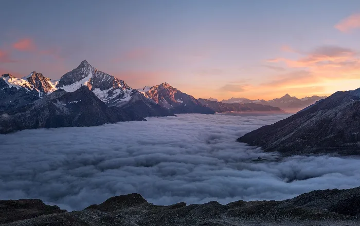 Alpine peaks rising above a sea of clouds at sunrise