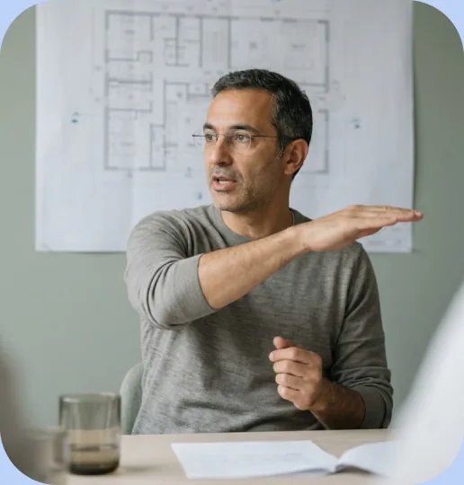 Man in glasses gesturing while explaining in front of floor plans pinned to a wall