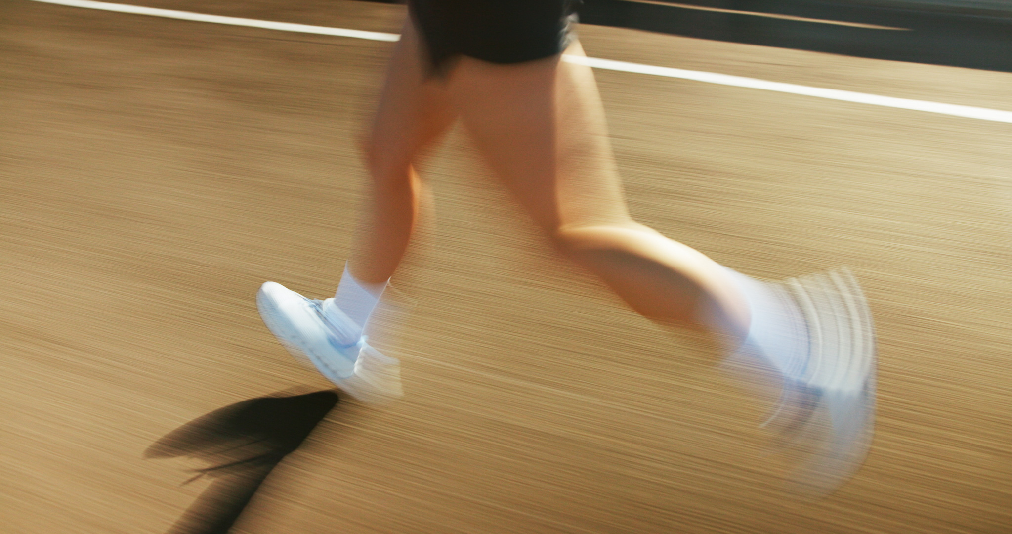 Blurred image of a person running in white sneakers and socks on a road with a painted white line.