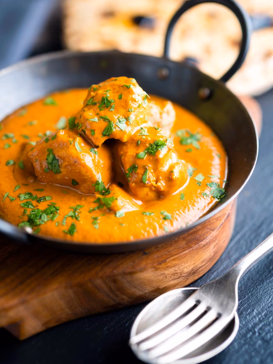 Chunks of meat in creamy orange sauce garnished with chopped herbs in a black bowl.