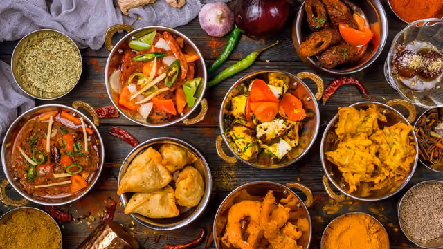 Assorted Indian dishes and spices arranged in bowls on a rustic wooden table.