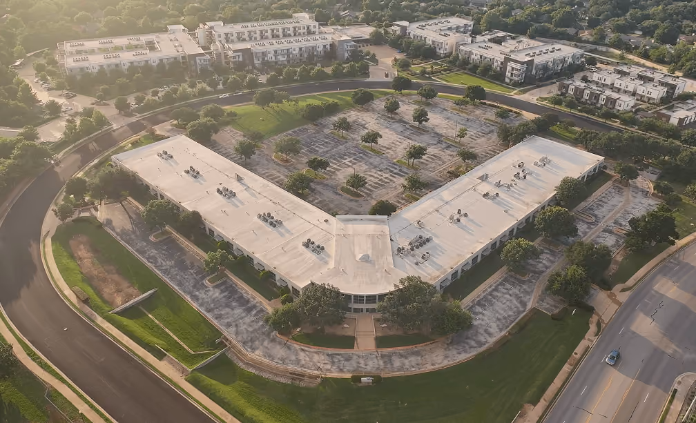 Aerial view of a V-shaped commercial building with empty parking lots surrounded by roads and greenery.