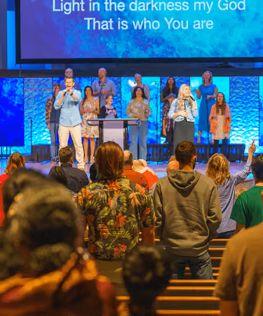 People worshipping in a church with singers on stage and lyrics projected above them.