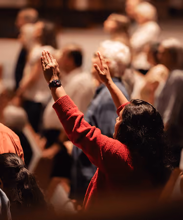 Woman in red sweater raising hands in a crowd during an indoor event.