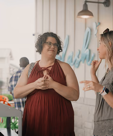 Two women engaged in conversation in a casual indoor setting with decorations in the background.