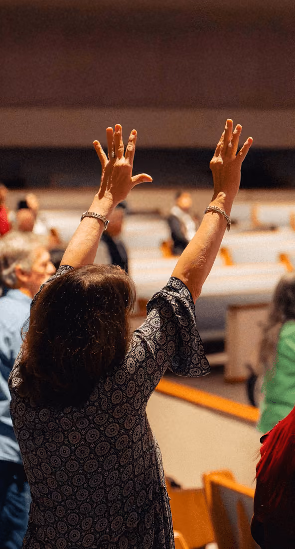 Person raising both hands with fingers spread in a seated audience setting.
