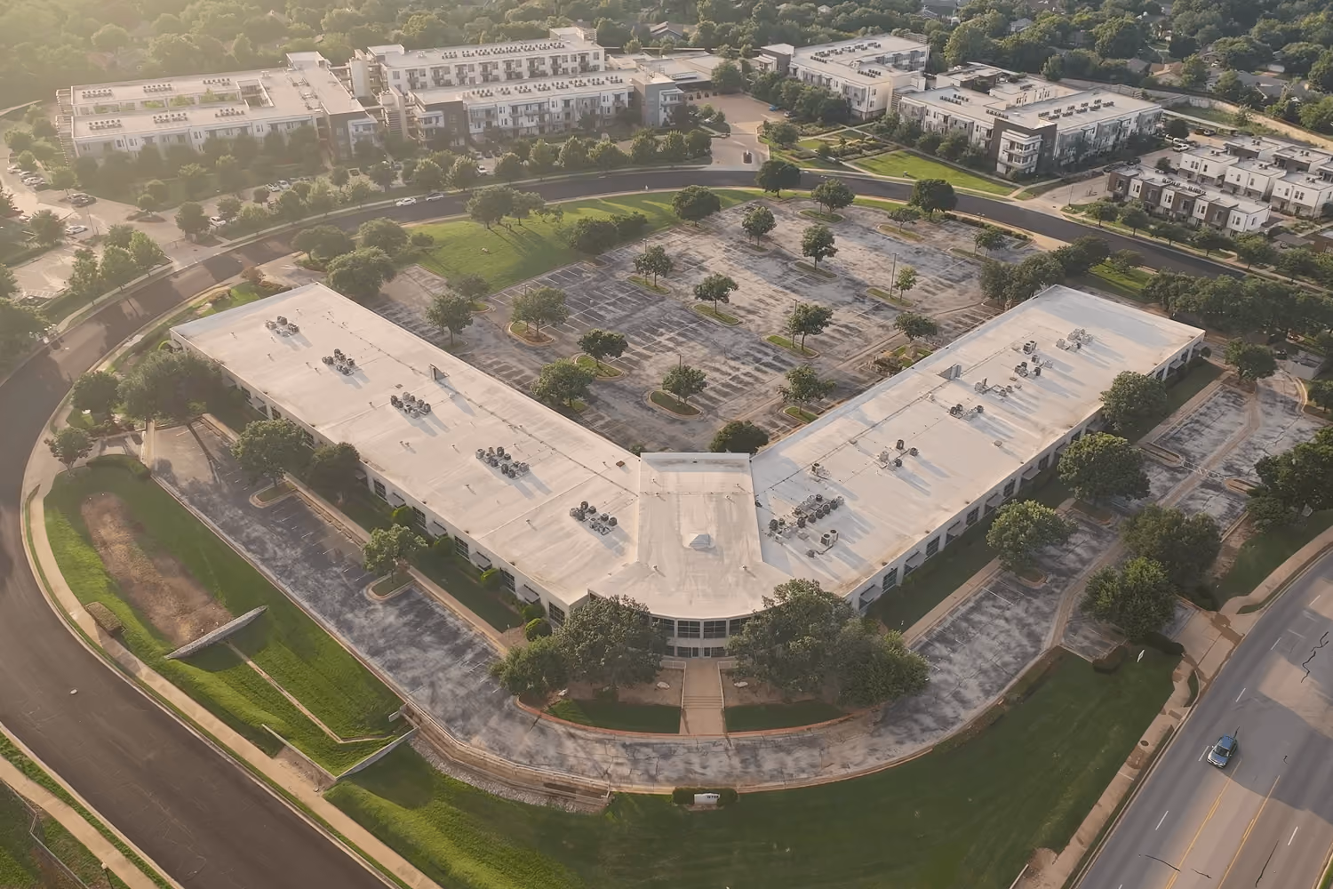 Aerial view of a large V-shaped commercial building with parking lots and surrounding greenery.