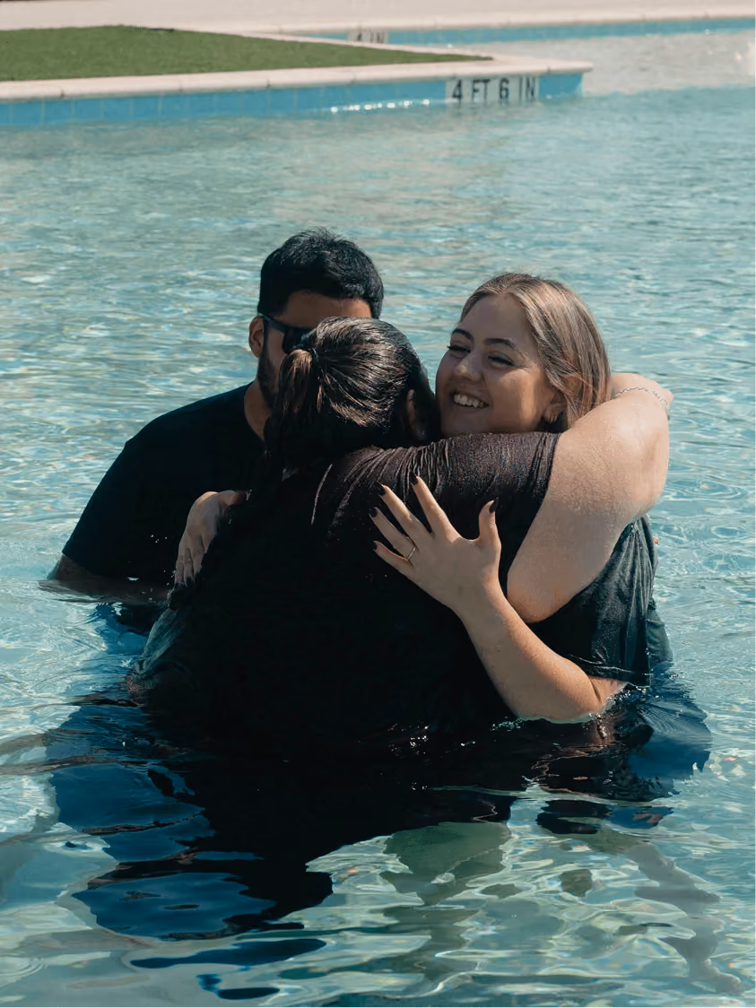 Three people hugging in a swimming pool near the poolside marked 4 feet 6 inches deep.