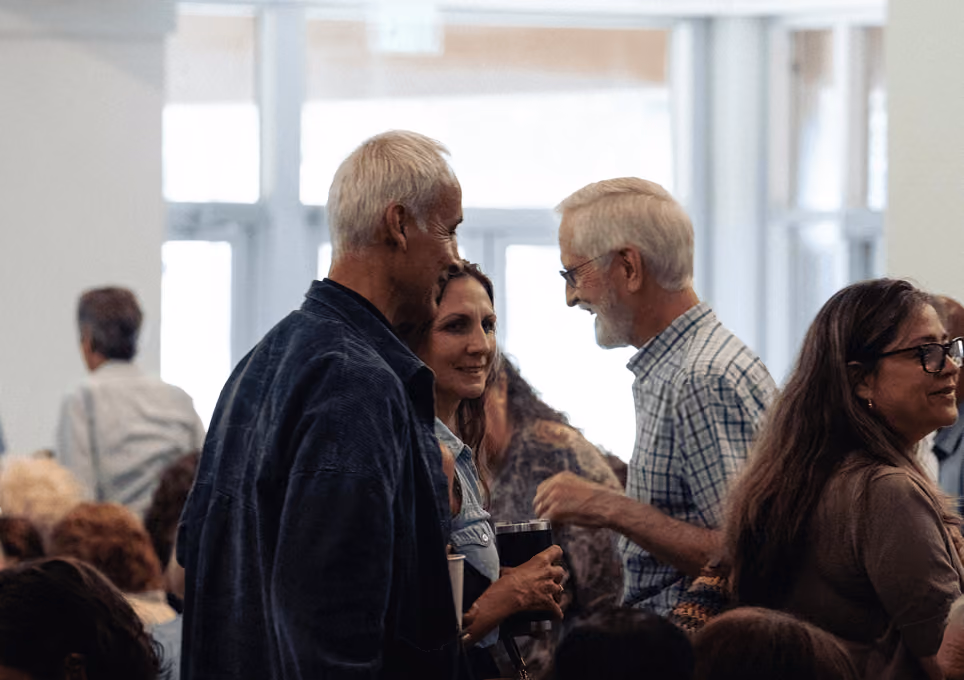 Group of adults socializing indoors, holding drinks and engaging in conversation.