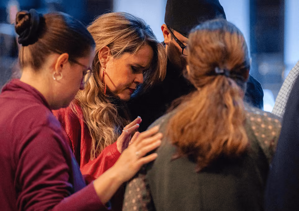 Group of people with heads bowed and eyes closed in shared moment of prayer or reflection.
