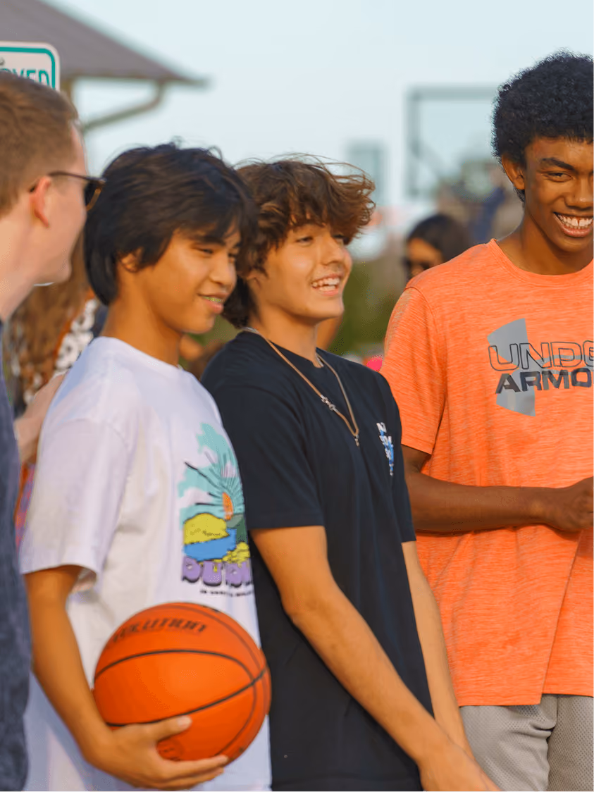 Group of smiling teenage boys standing outdoors, one holding a basketball.