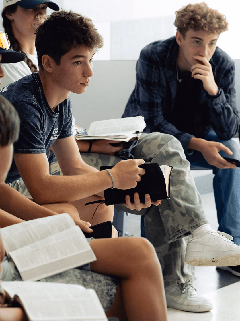 Group of teenagers sitting in a circle reading books and holding a tablet, engaged in discussion.