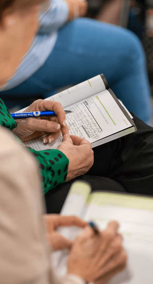 Two adults writing notes in notebooks during a meeting or class setting.