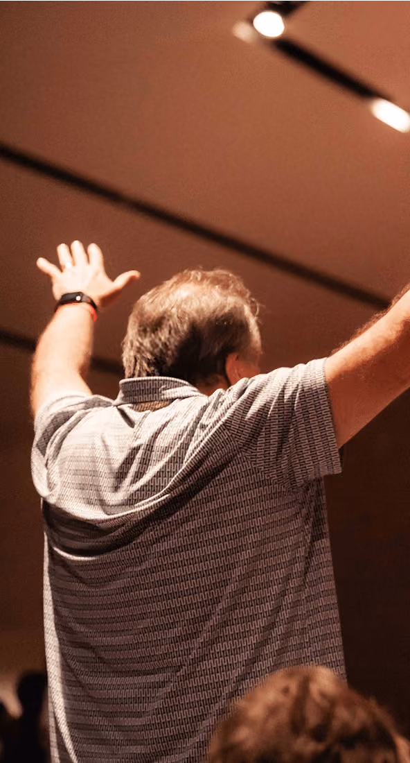 Man with outstretched arms seen from behind indoors under warm lighting.