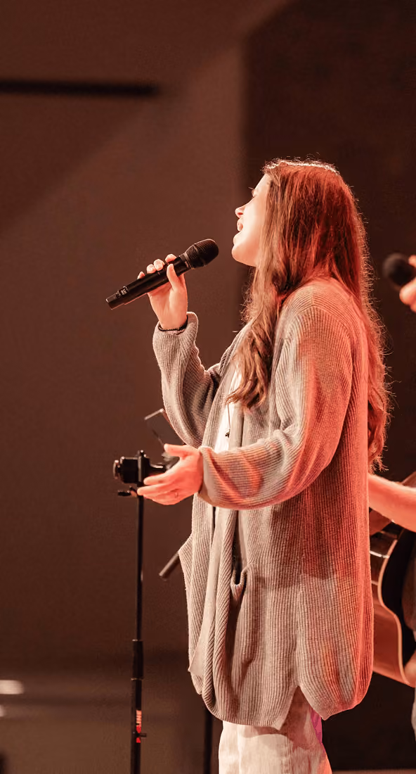 Woman singing into microphone on stage with a guitar player beside her.