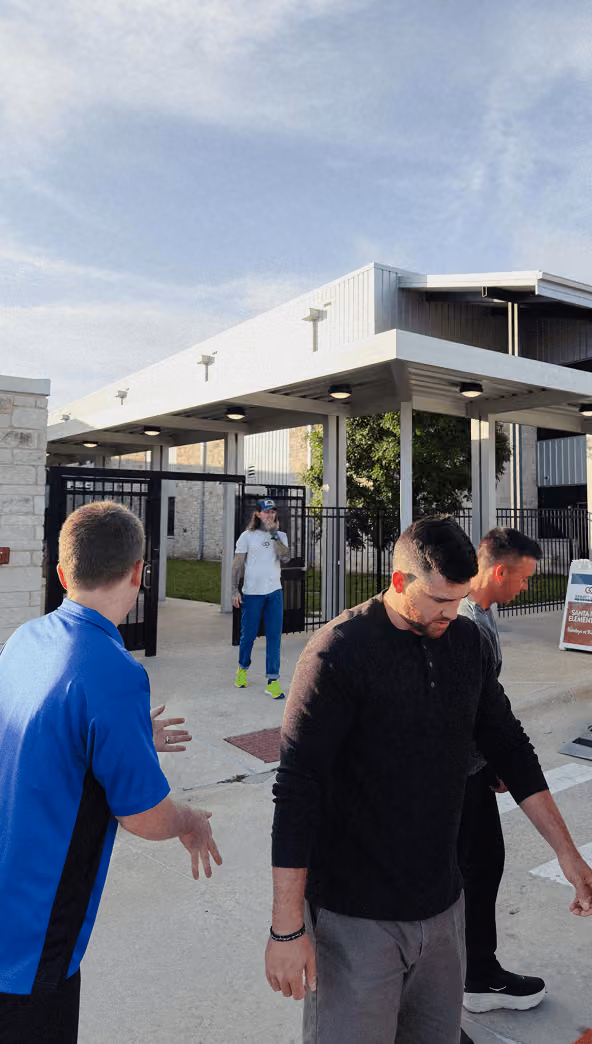Three men standing and talking outside near a modern building with a covered walkway.