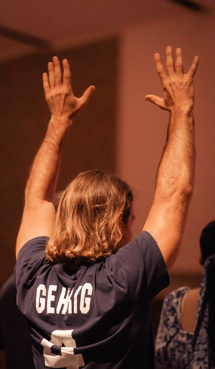 Person with long hair raising both hands, wearing a blue shirt with the name 'GEHRIG' on the back.