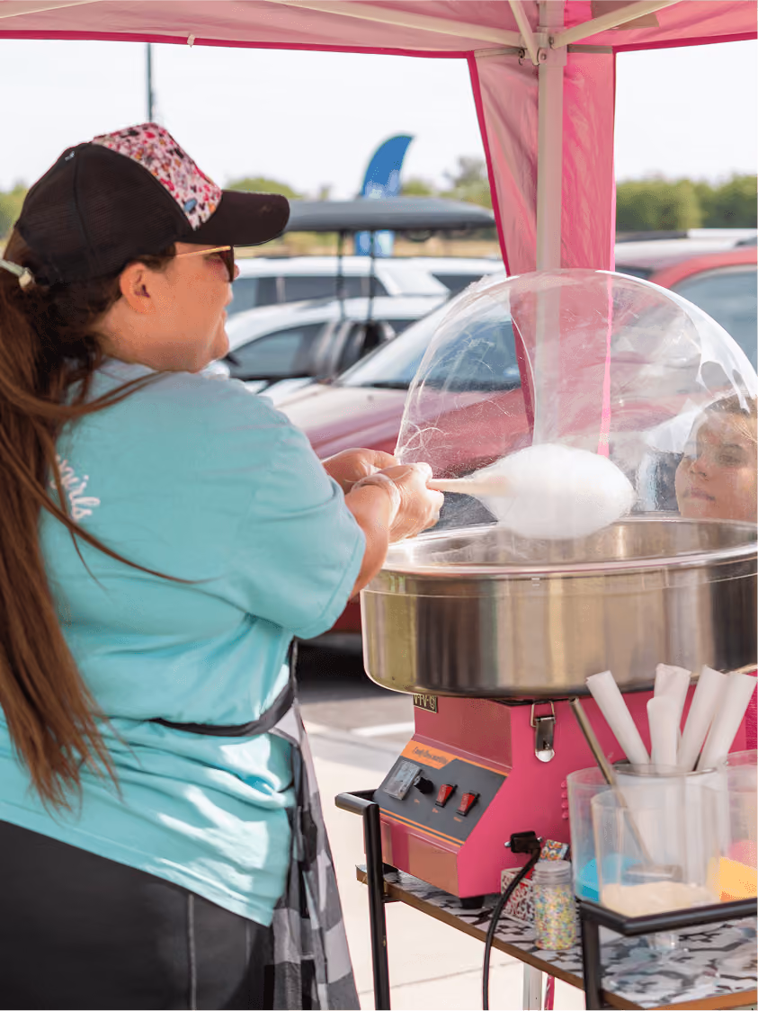 Woman making cotton candy with a pink cotton candy machine under a pink canopy outdoors.