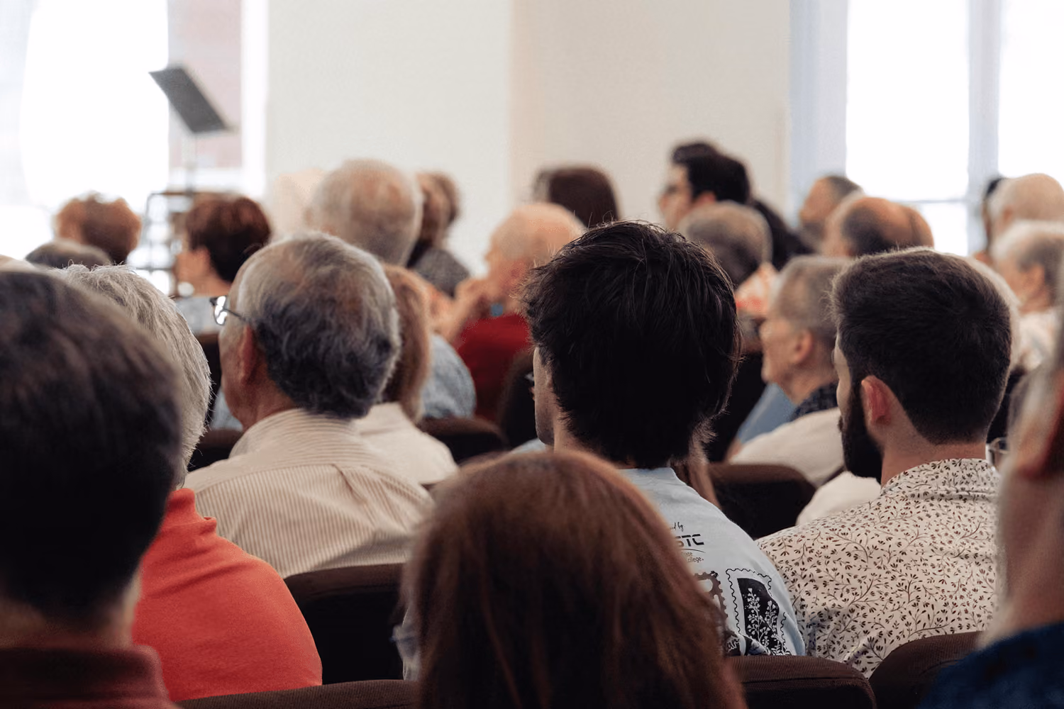 Audience of various ages seated and facing forward in a well-lit room.