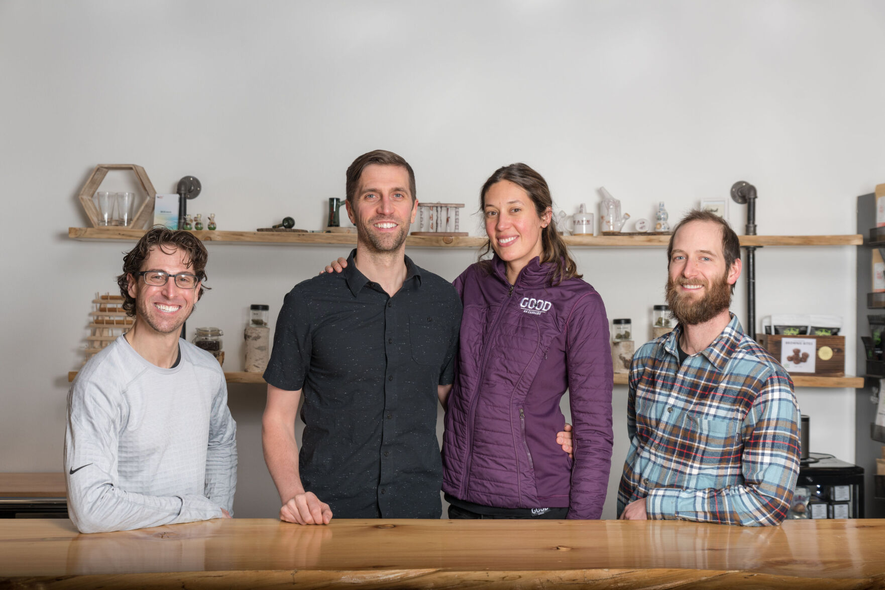 Four members of the GOOD Cannabis team smiling behind the wooden counter at the Fairbanks shop