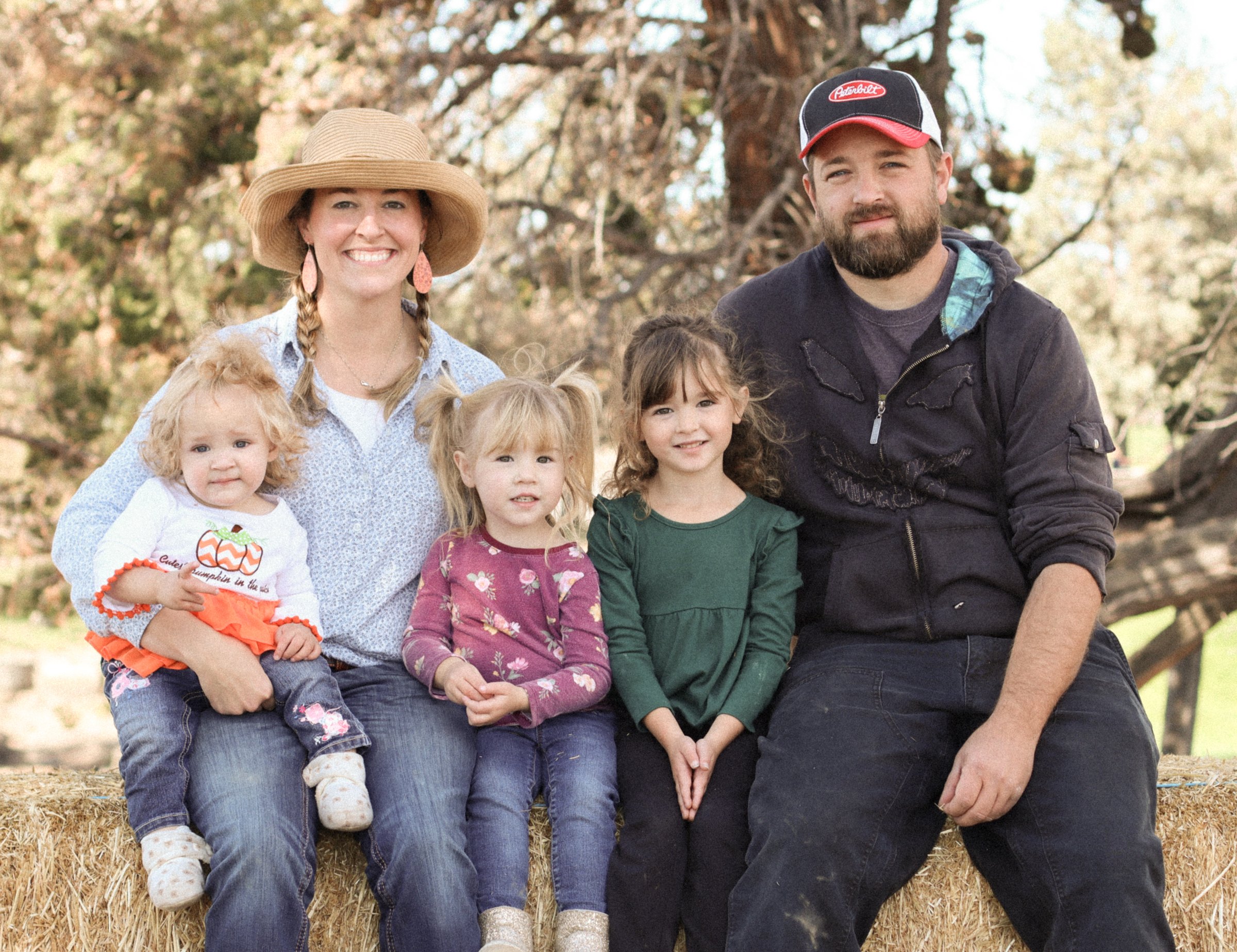 The family behind Raven's View Farm seated on a hay bale with their three young daughters in Powell Butte, Oregon