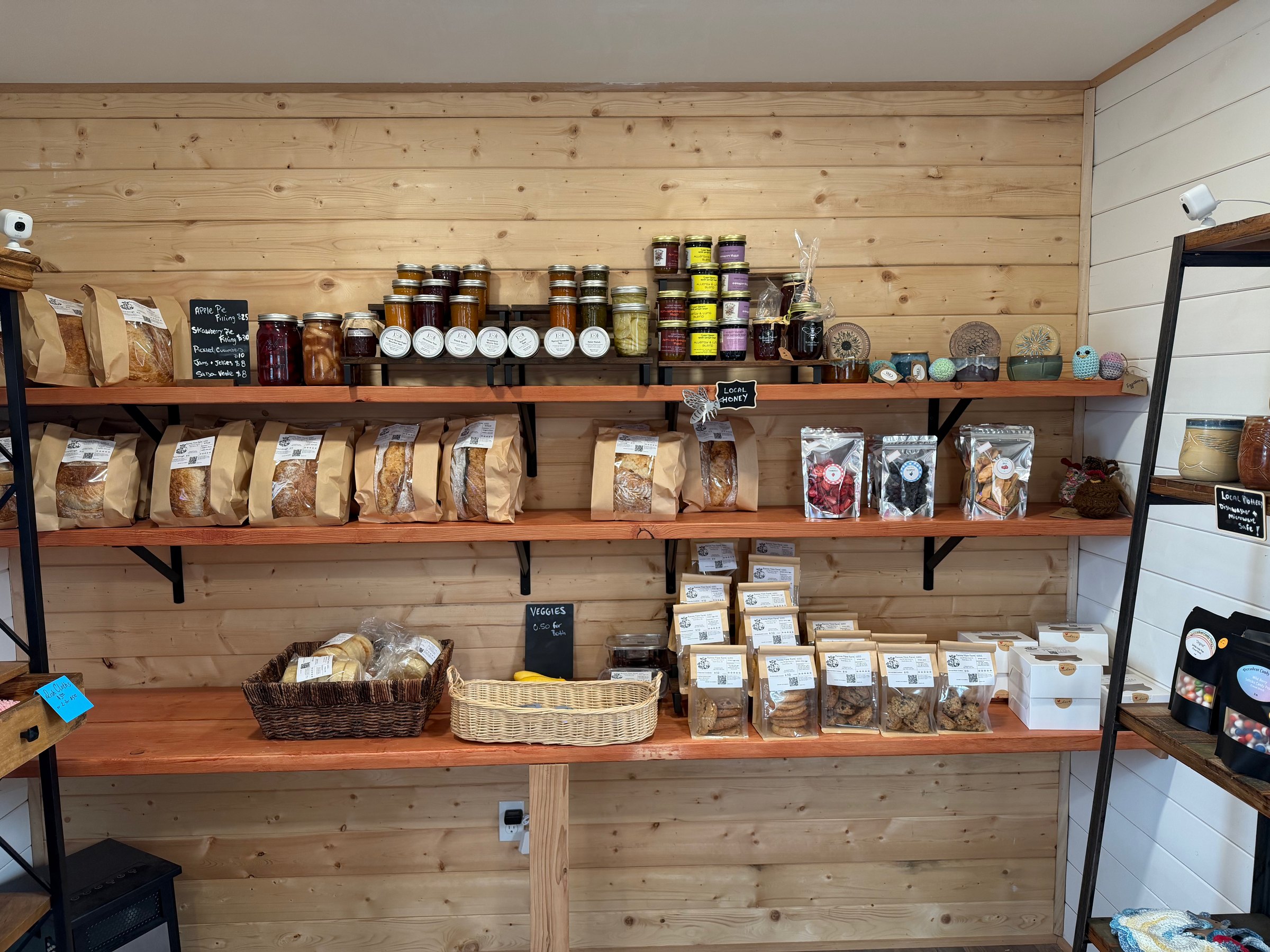 Farm store shelves lined with canned jams, dried goods and cookies, alongside local honey and handmade pottery