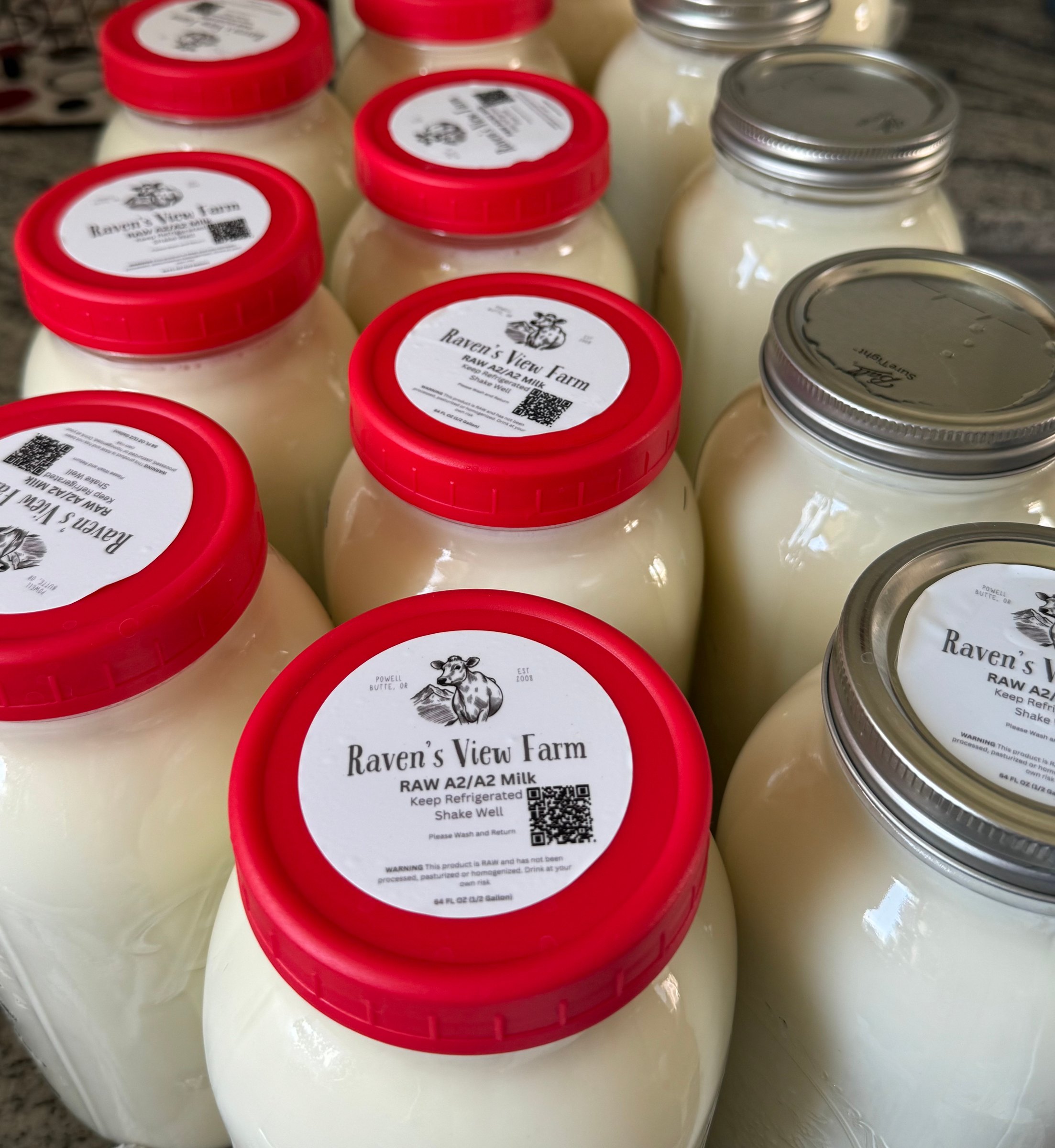 Close-up of Raven's View Farm raw A2/A2 milk jars with red lids and the farm's cow-and-mountain logo label