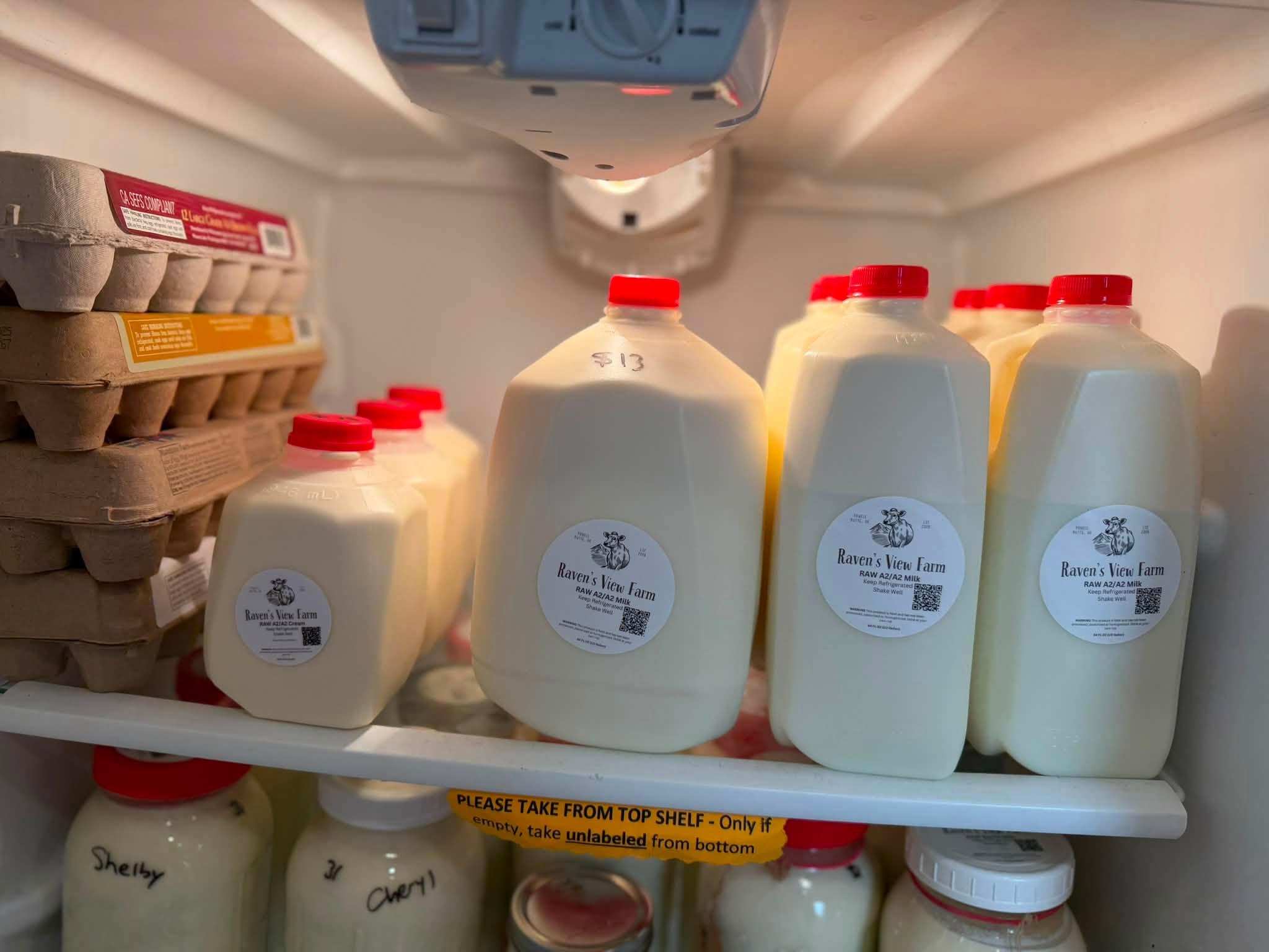 The farmstand pickup fridge stocked with cartons of eggs and half gallons of Raven's View Farm raw milk
