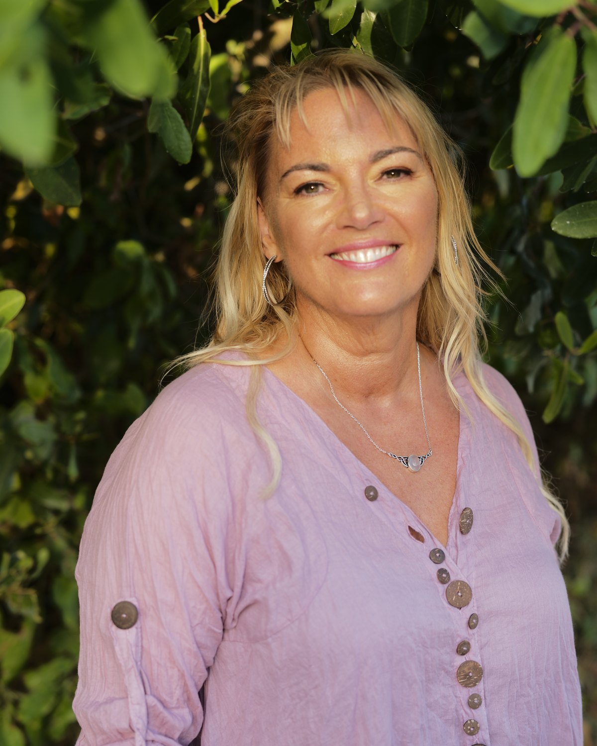 Pauline McGuire smiling outdoors in front of green foliage