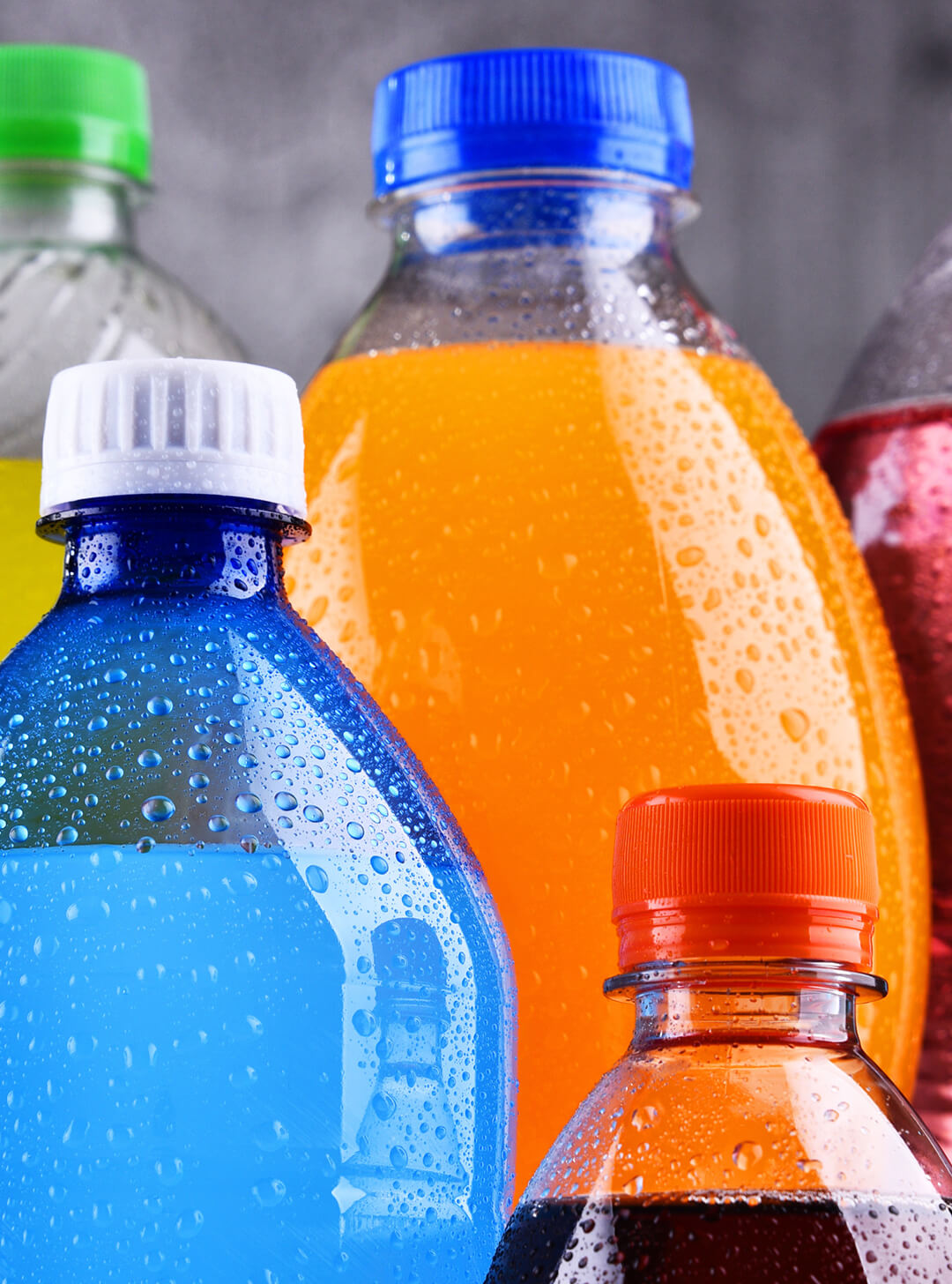 Close-up of various colorful cold beverage bottles with condensation droplets on them.