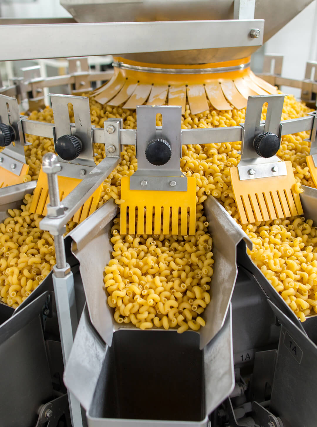 Macaroni pasta being dispensed into slots of an industrial packaging machine.