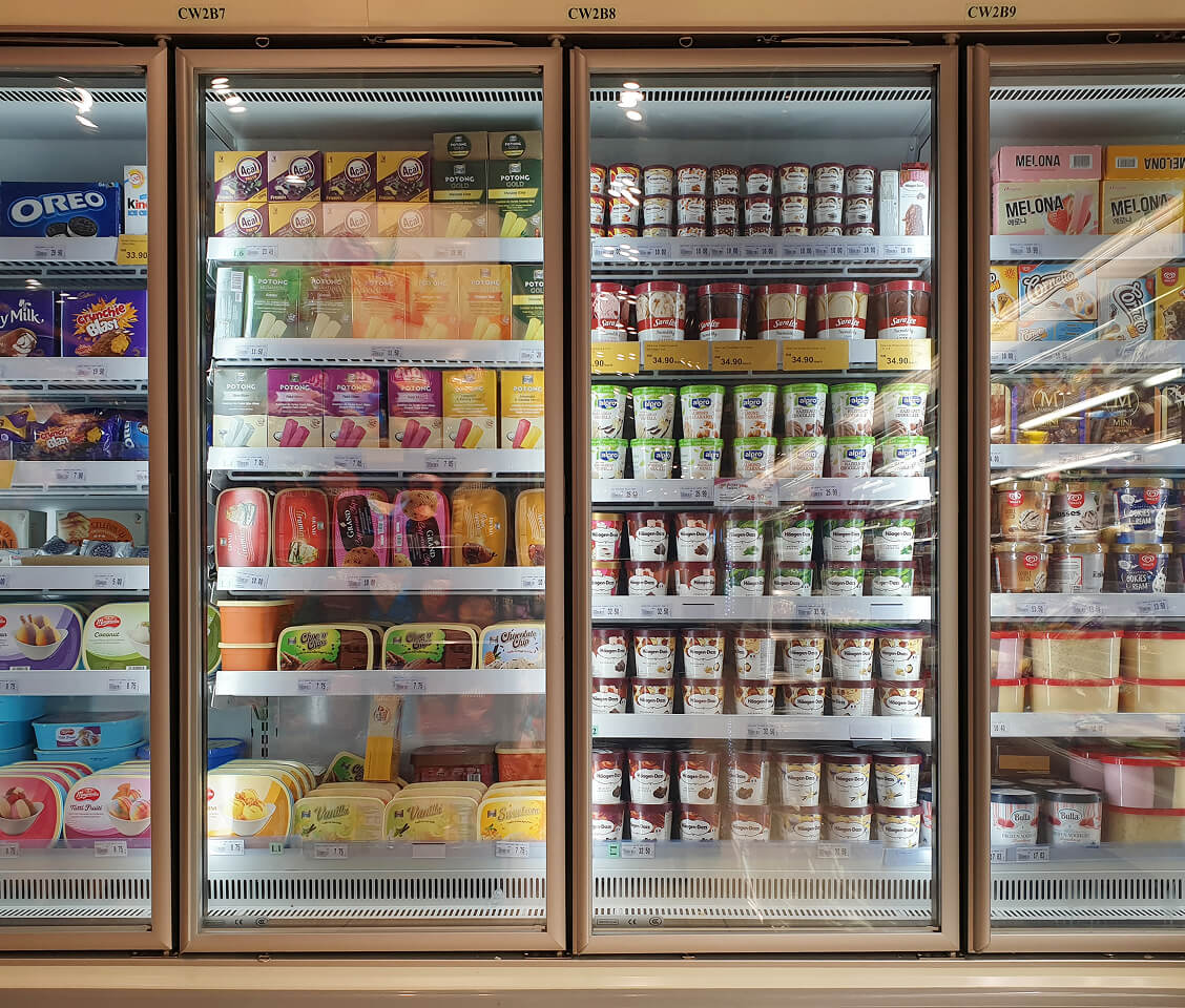 Supermarket freezer with various ice cream brands and frozen desserts displayed on shelves.