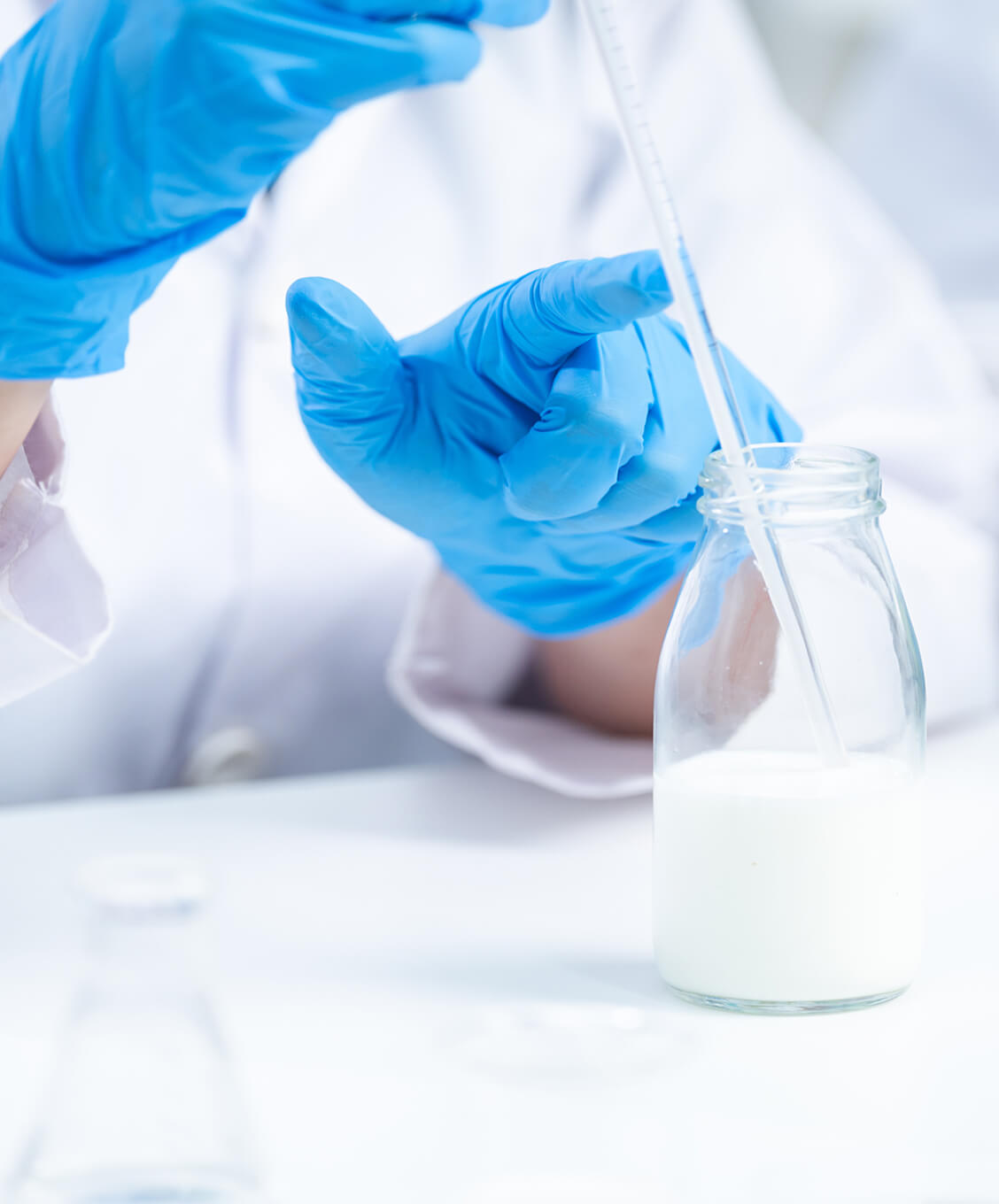 Scientist wearing blue gloves uses a pipette to extract liquid from a glass bottle with milk.